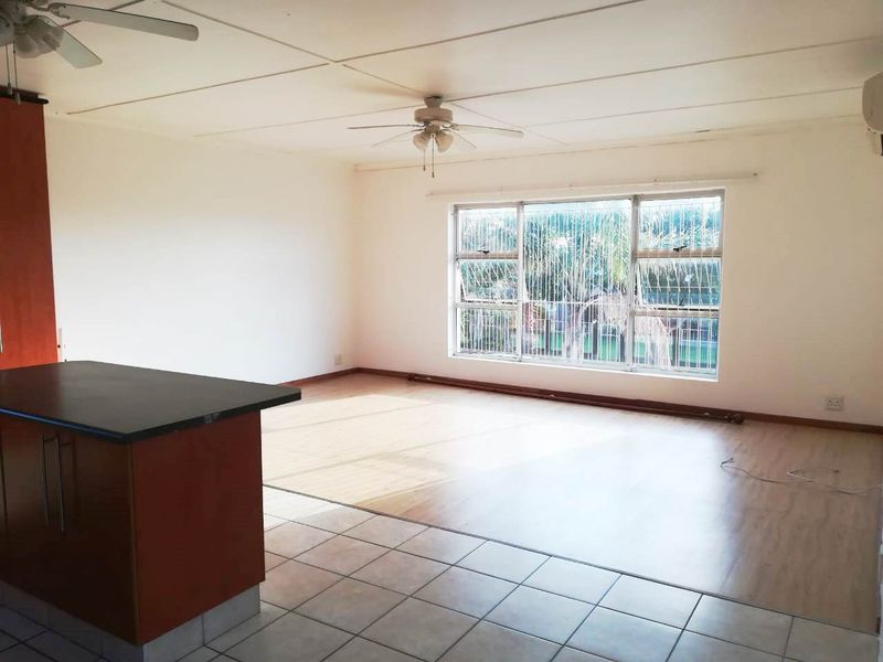 Spacious open-plan living area featuring a kitchen island, dual flooring finishes, ceiling fans, and large windows with security bars.