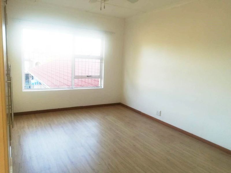 An empty bedroom featuring laminate flooring, a built-in cupboard, and a ceiling fan, with natural light entering through a window with security bars.