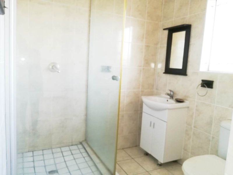 A functional bathroom featuring a glass-enclosed shower, a vanity cabinet with a basin, and neutral wall and floor tiling.