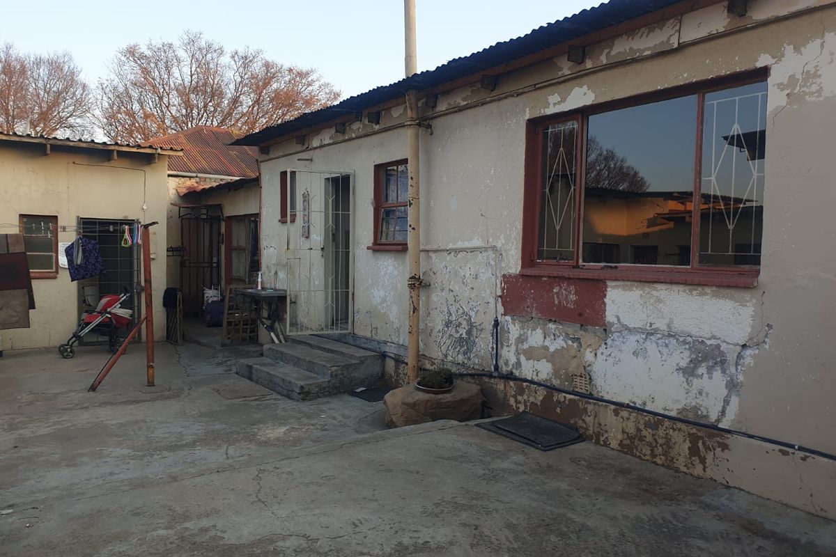 Rear exterior view of the property showing a concrete courtyard, weathered building facade, and metal security window bars.
