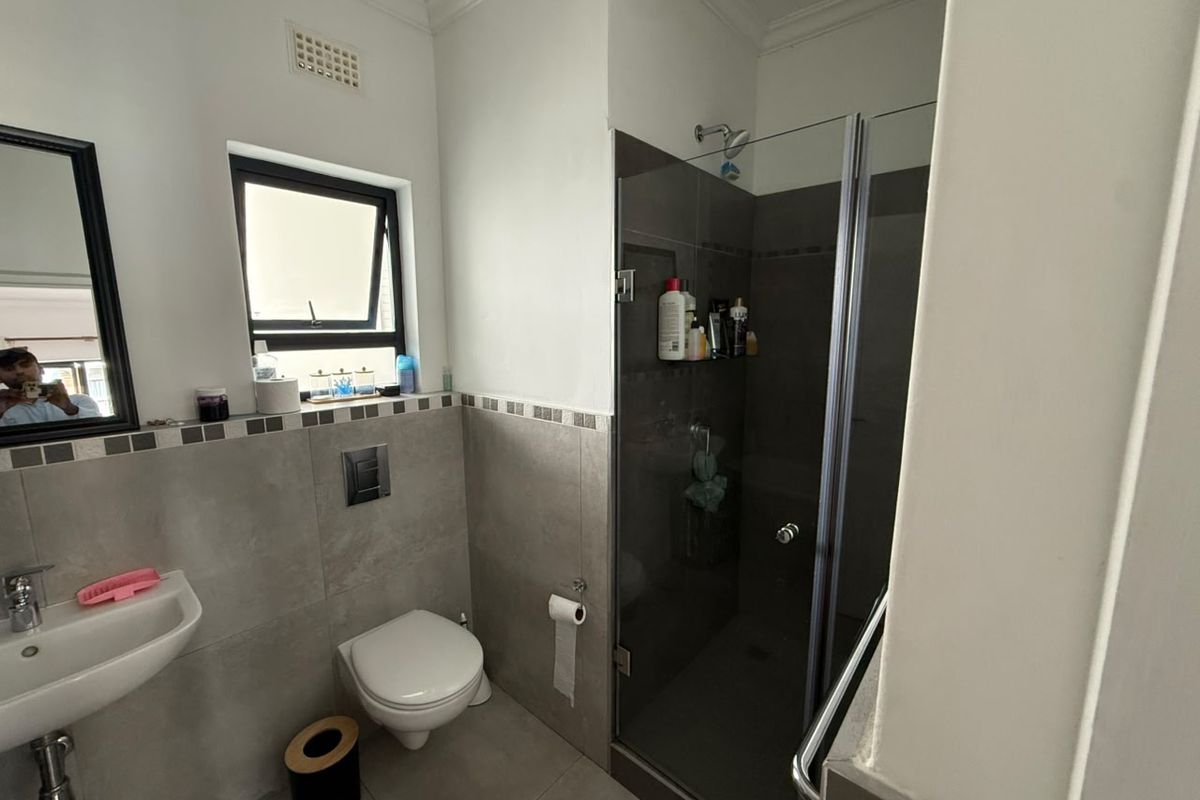 A modern bathroom featuring a glass-enclosed shower, wall-mounted toilet, and a pedestal basin with neutral grey tiling.