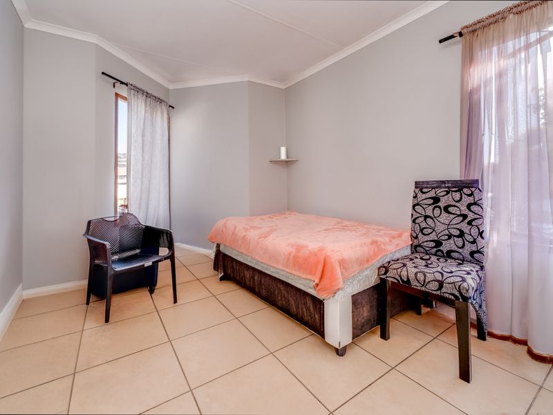 A bedroom featuring neutral wall paint, tiled flooring, and dual windows with curtain rods.