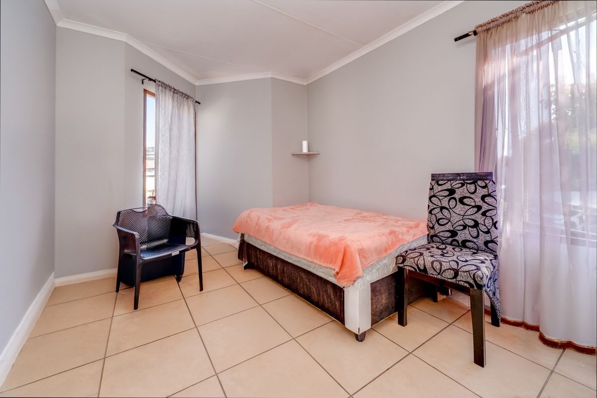A bedroom featuring neutral wall paint, tiled flooring, and dual windows with curtain rods.