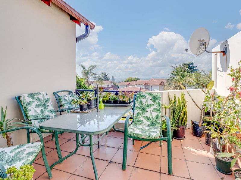 A sunny, tiled balcony featuring a parapet wall and elevated views, providing a pleasant outdoor space for relaxation.