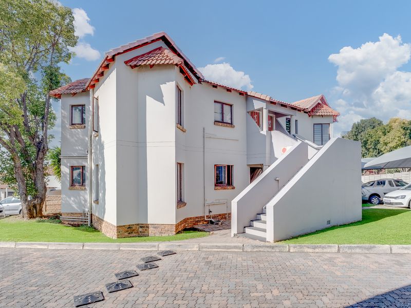 A well-maintained townhouse exterior featuring a tiled roof, concrete staircase, and paved driveway access within a residential complex.