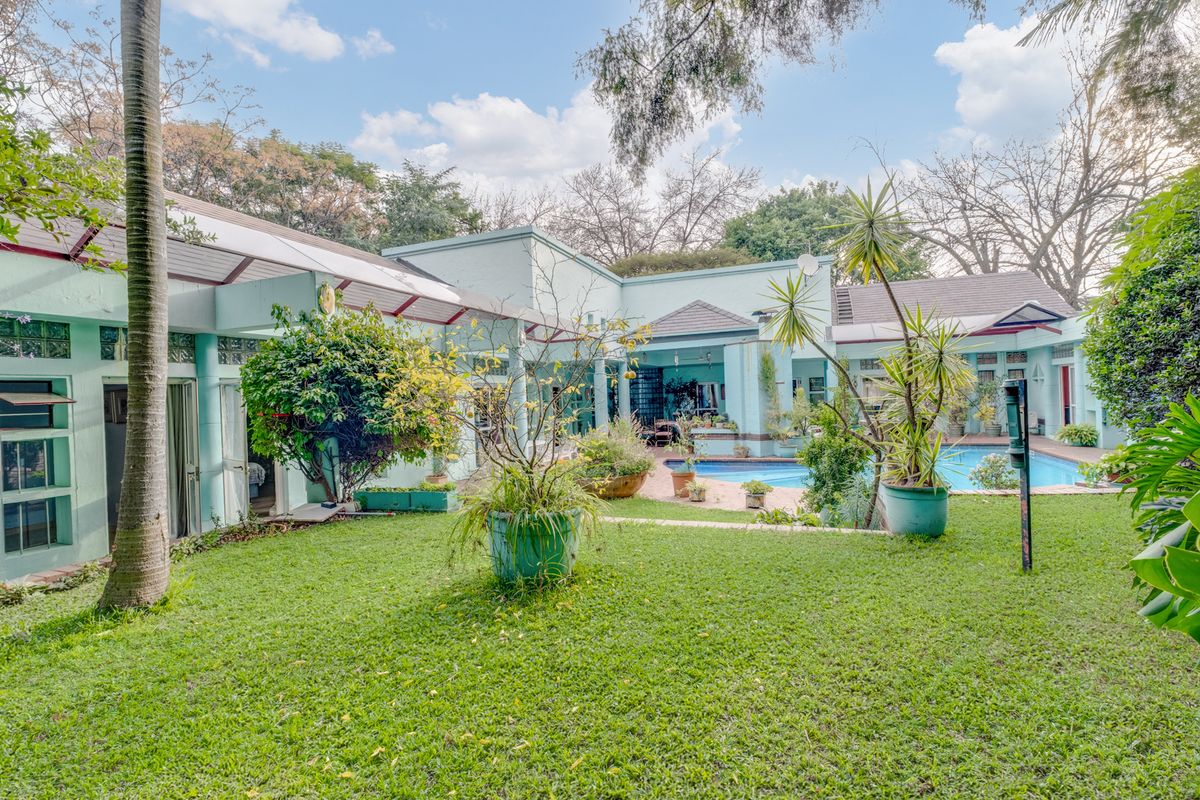 Rear view of the property featuring a swimming pool, covered patio area, and established garden with mature trees.
