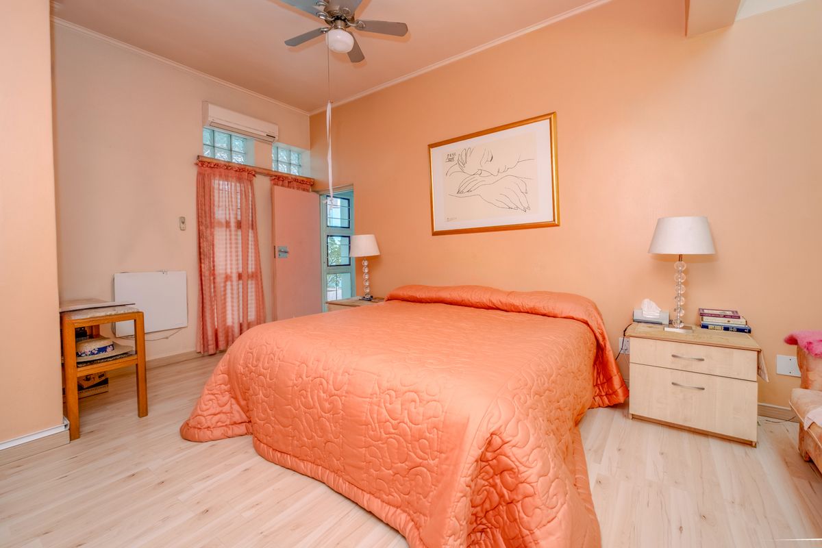 A bedroom featuring laminate flooring, a ceiling fan, and a wall-mounted split-system air conditioner with glass block accent windows.