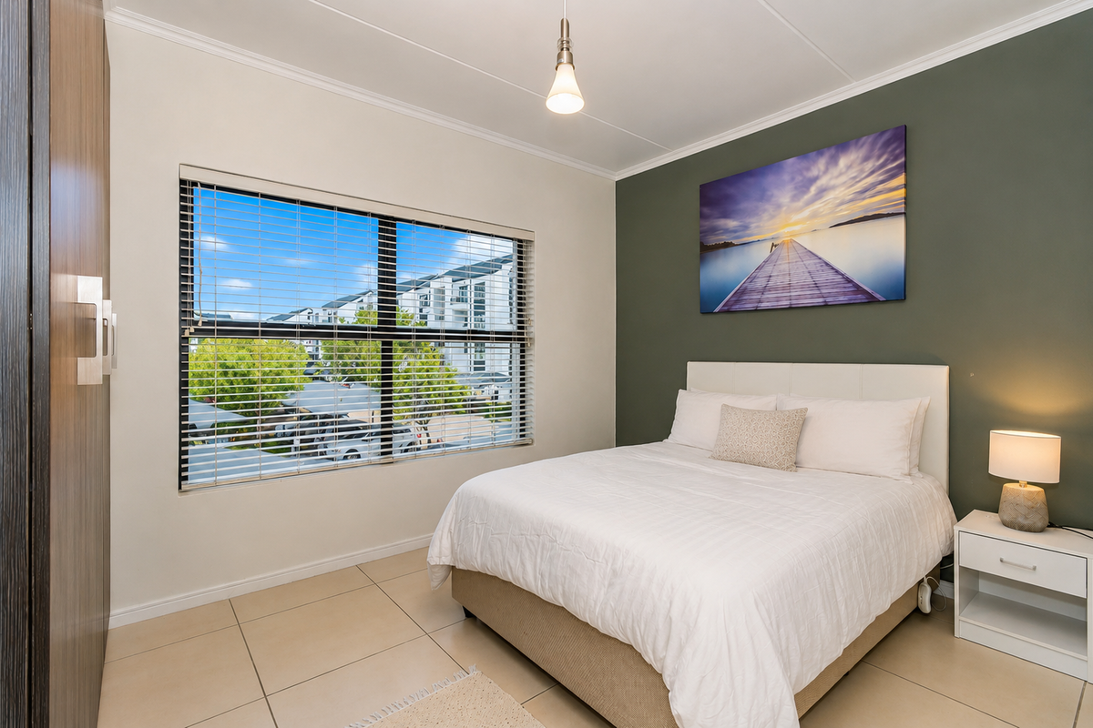 A well-maintained bedroom featuring tiled flooring, a built-in wardrobe, and a large window with blinds, offering a bright and comfortable living space.