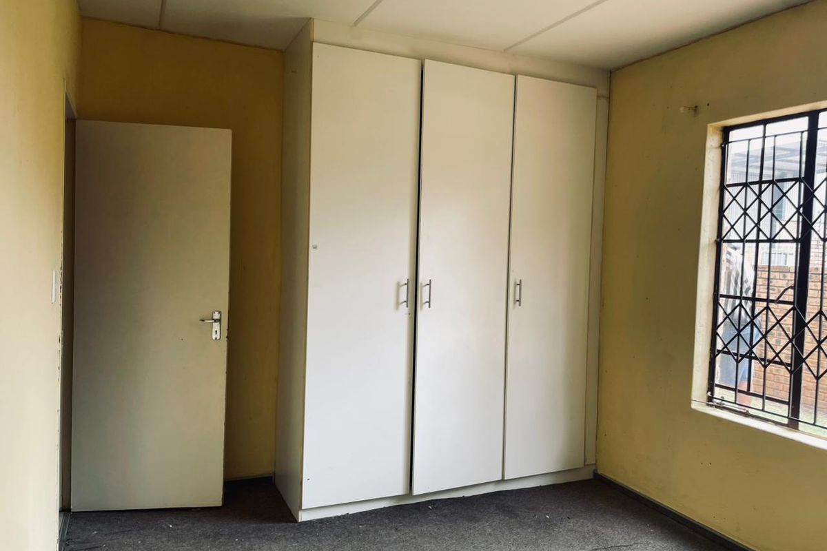 A bedroom featuring built-in white cabinetry, carpeted flooring, and a window secured with metal burglar bars.
