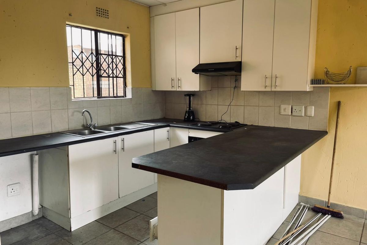 A functional kitchen featuring white cabinetry, dark laminate countertops, a built-in extractor fan, and tiled flooring with a breakfast bar area.