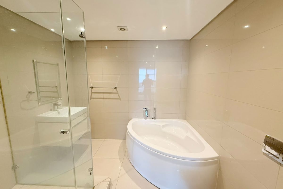 Modern bathroom featuring a corner bathtub, glass-enclosed shower, wall-mounted vanity, and neutral floor-to-ceiling tiling.