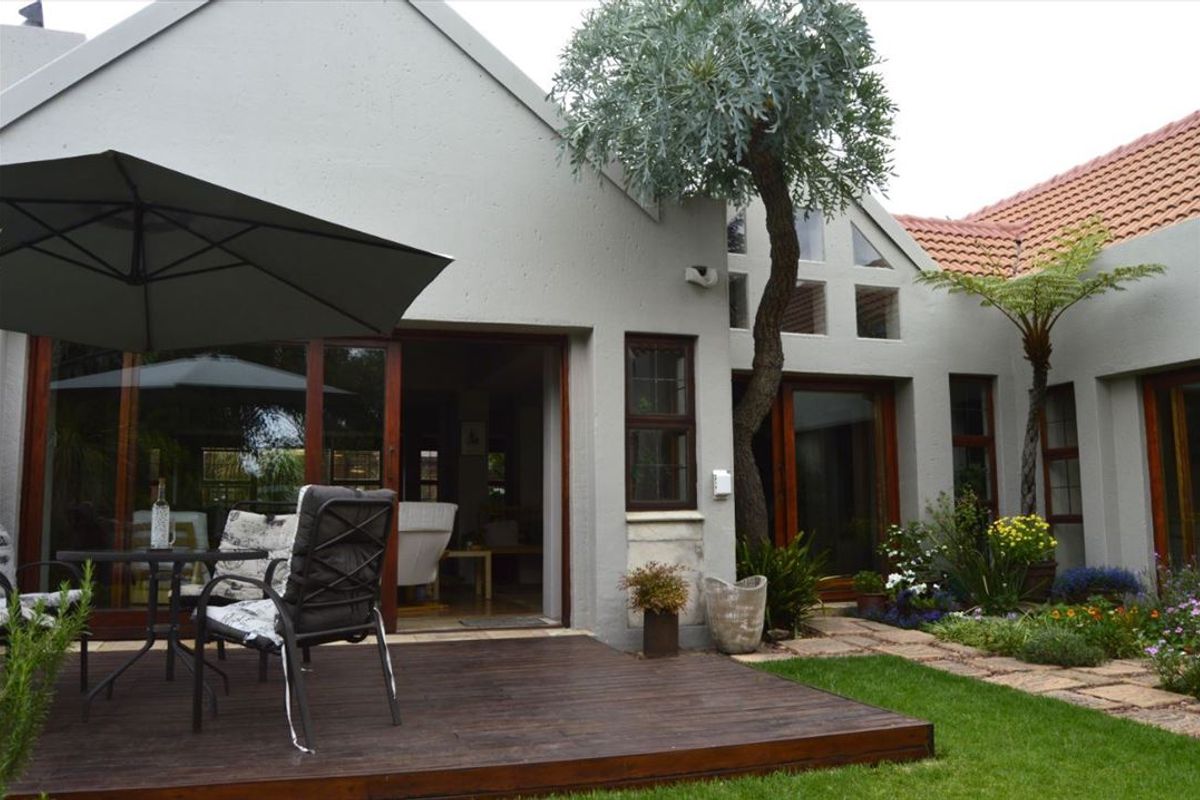 A well-maintained rear exterior view featuring a timber deck, landscaped garden, and large glass sliding doors providing seamless indoor-outdoor flow.