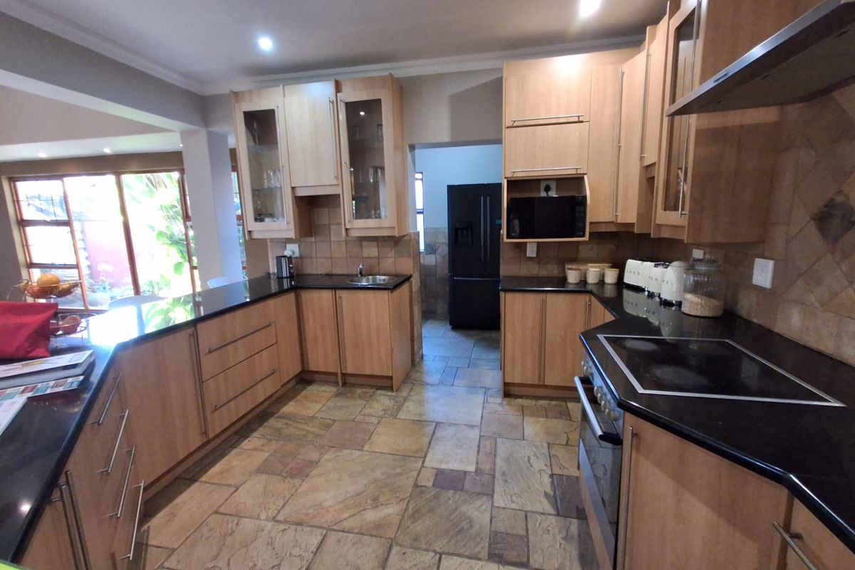 A functional kitchen featuring light wood cabinetry, dark granite countertops, integrated oven and hob, and natural stone floor tiles.