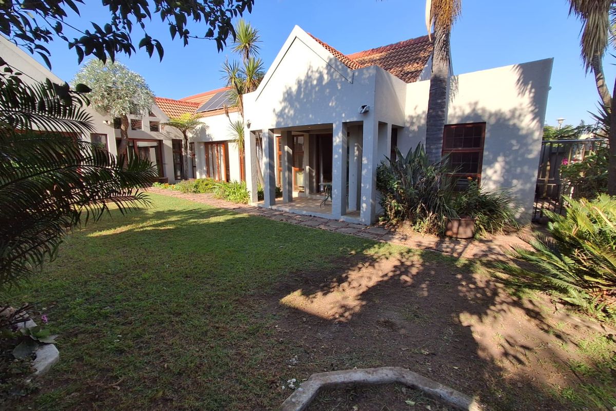 A view of the rear garden and patio area featuring a tiled covered porch, established landscaping, and a pitched roof structure.