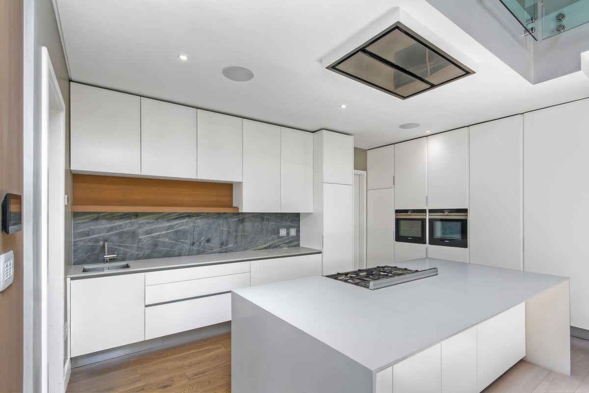 Modern kitchen featuring sleek white cabinetry, stone countertops, a central island with a gas hob, and integrated double ovens.