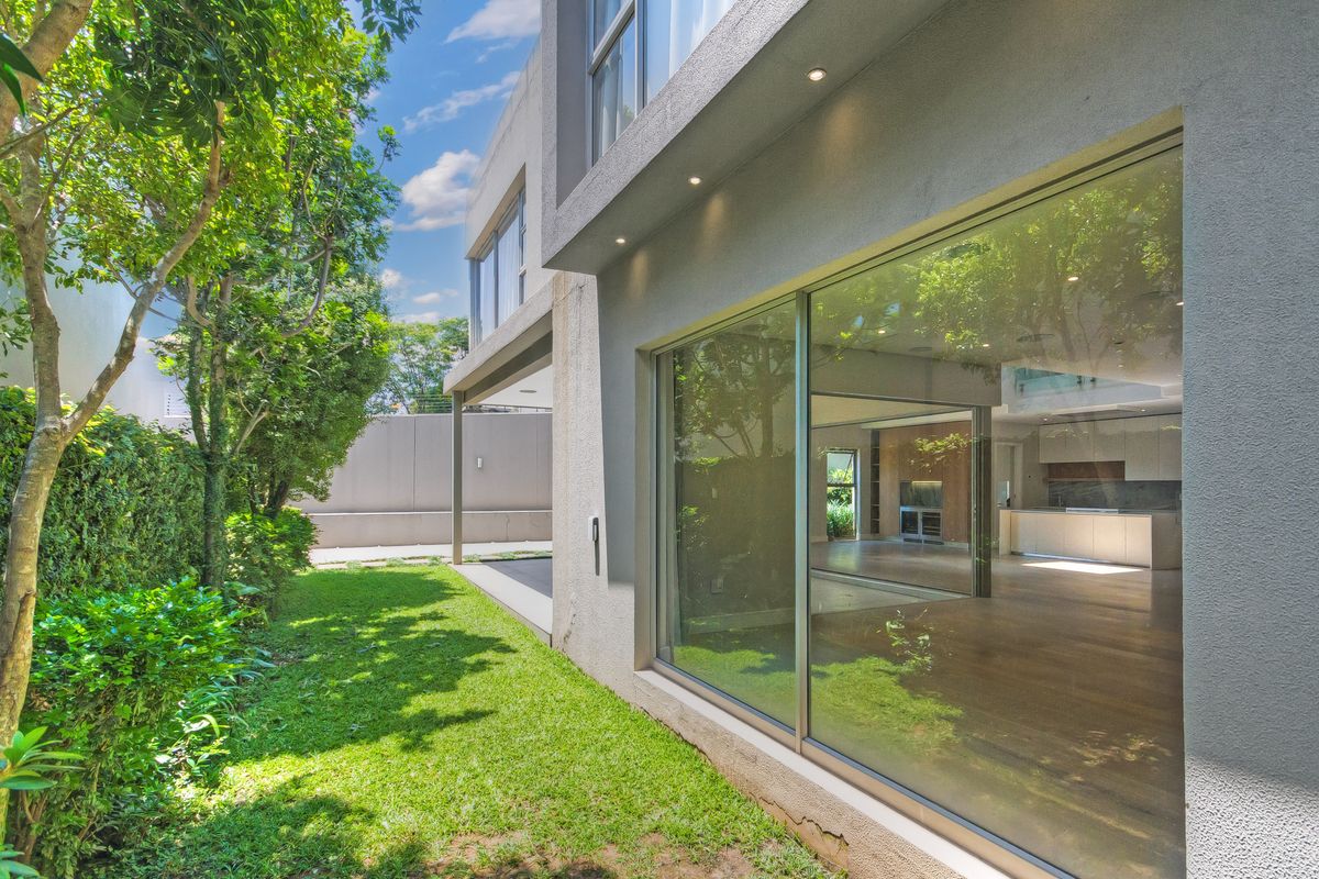 A view of the rear exterior of the cluster home, featuring a landscaped garden, large sliding glass doors, and recessed exterior lighting.