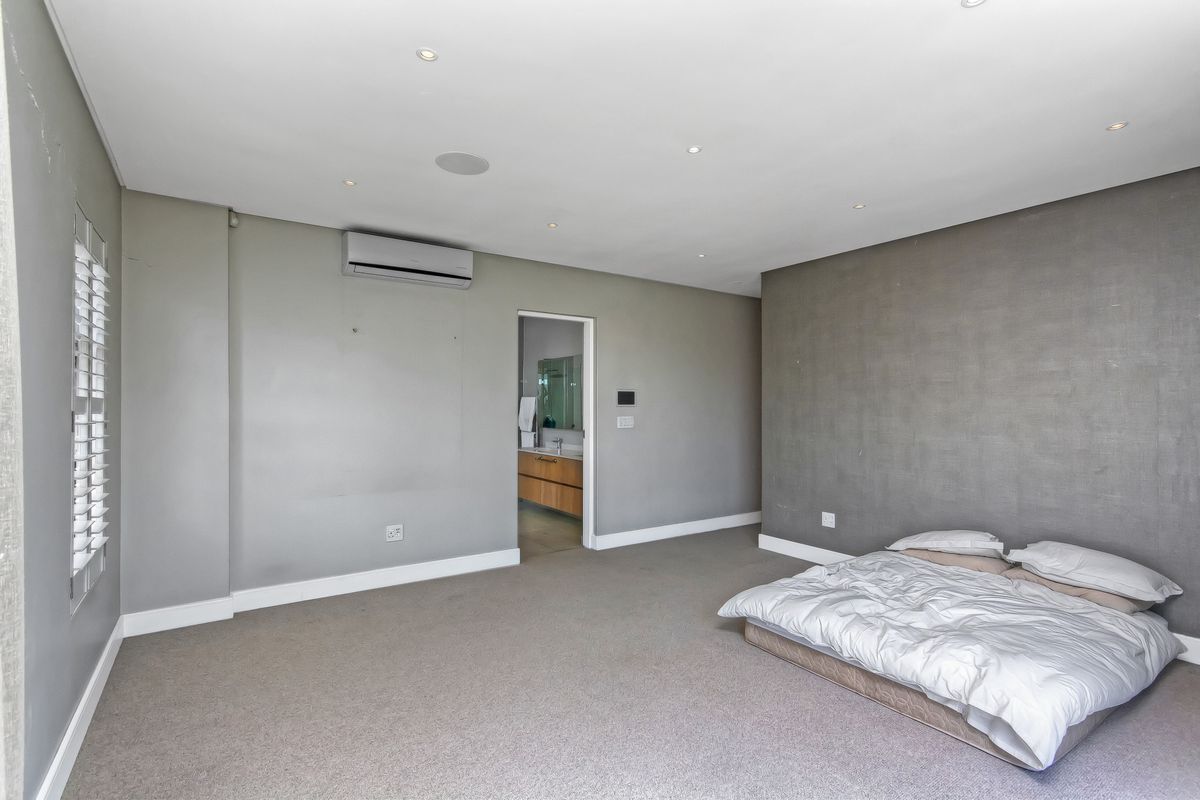 Spacious bedroom featuring neutral grey walls, recessed ceiling lighting, a wall-mounted air conditioning unit, and an en-suite bathroom entrance.