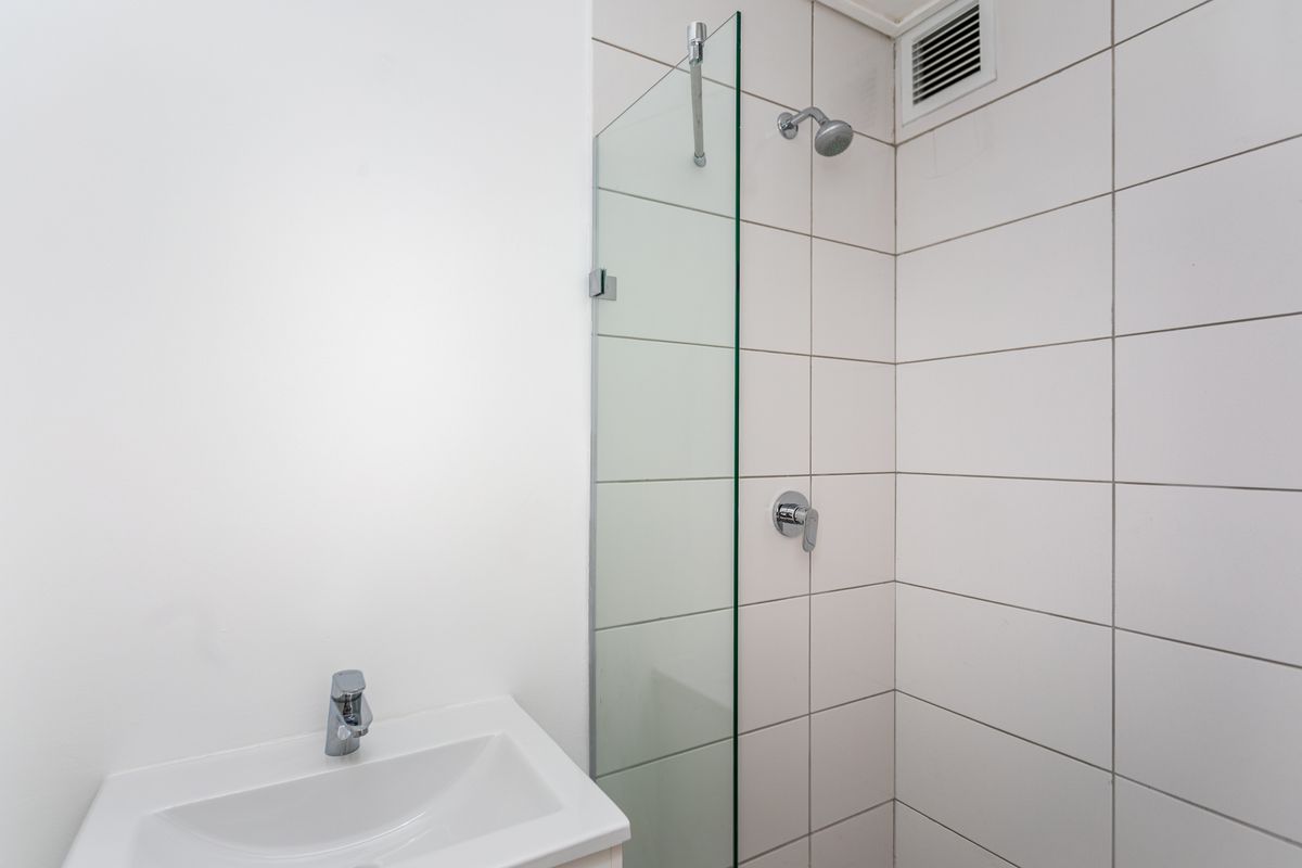 A clean, modern bathroom featuring a glass shower screen, wall-mounted shower head, and a white vanity basin with chrome faucet.
