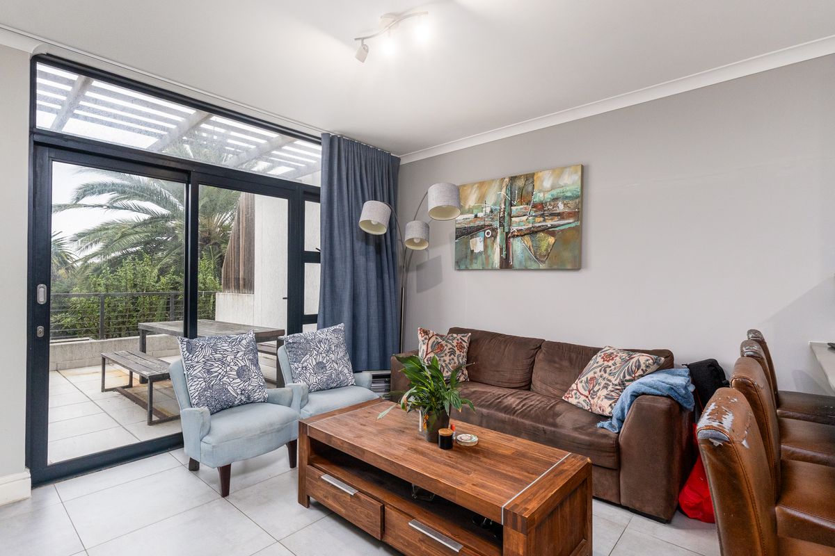 A bright living room featuring large sliding glass doors that open onto a patio, with neutral tiled flooring and modern track lighting.