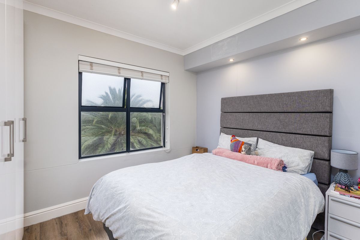 A well-lit bedroom featuring laminate flooring, a built-in wardrobe, and a large window with a view of greenery.