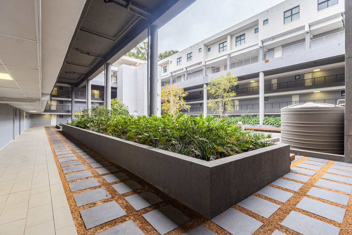 A well-maintained communal courtyard area featuring a large raised planter box, paved pathways, and a water storage tank within an apartment complex.