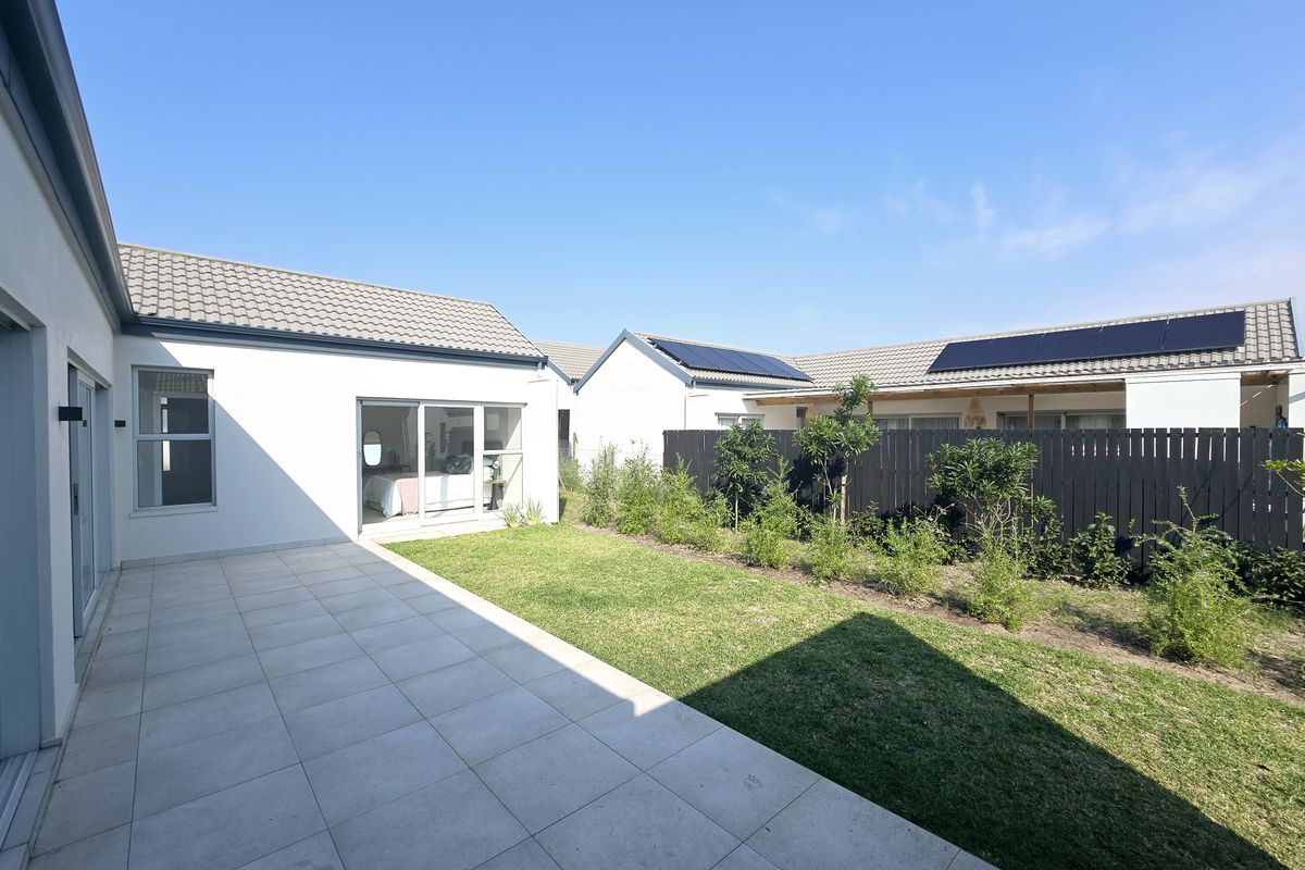 A well-maintained rear exterior featuring a tiled patio, manicured lawn, privacy fencing, and solar panels installed on the roof.