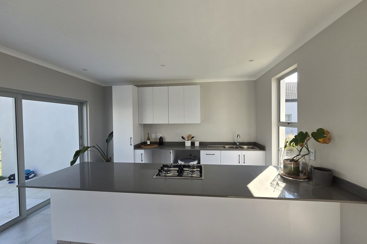 Modern kitchen featuring a central island with a gas hob, stone countertops, ample cabinetry, and direct access to the outdoor patio area.