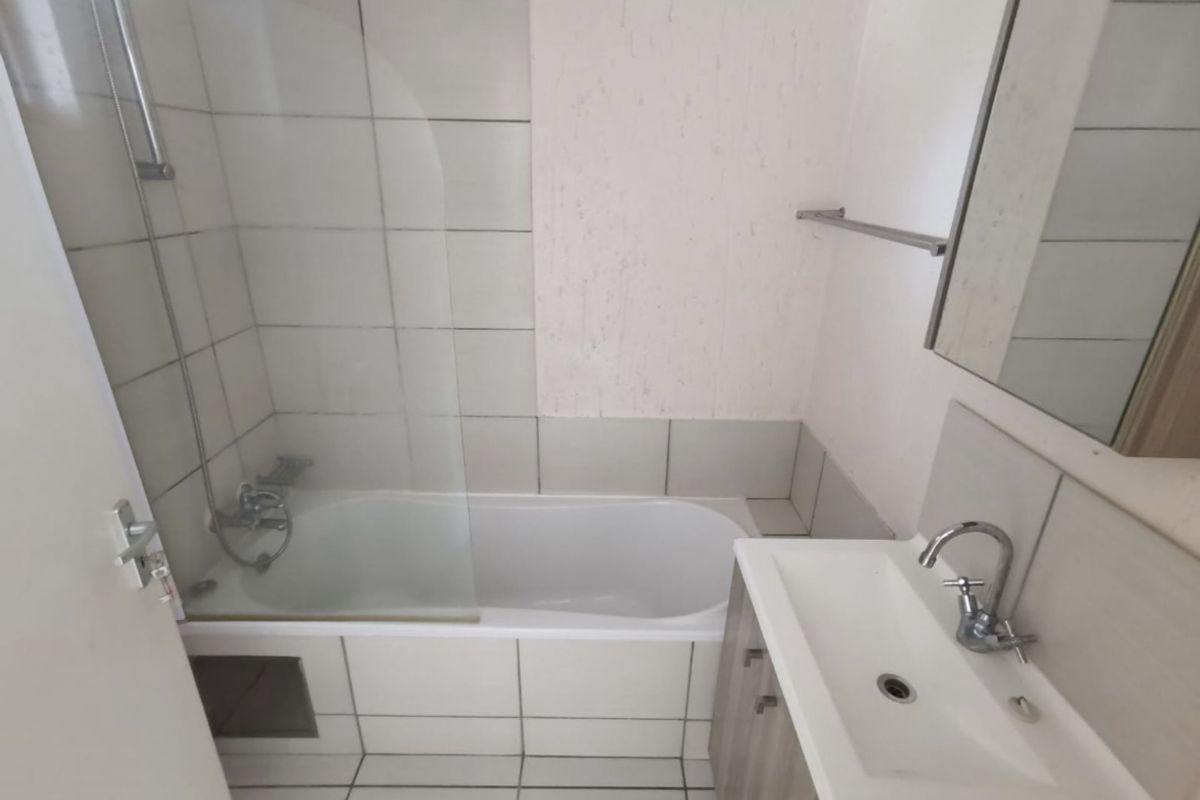 A functional bathroom featuring a bathtub with a glass shower screen, a vanity basin, and tiled flooring and walls.