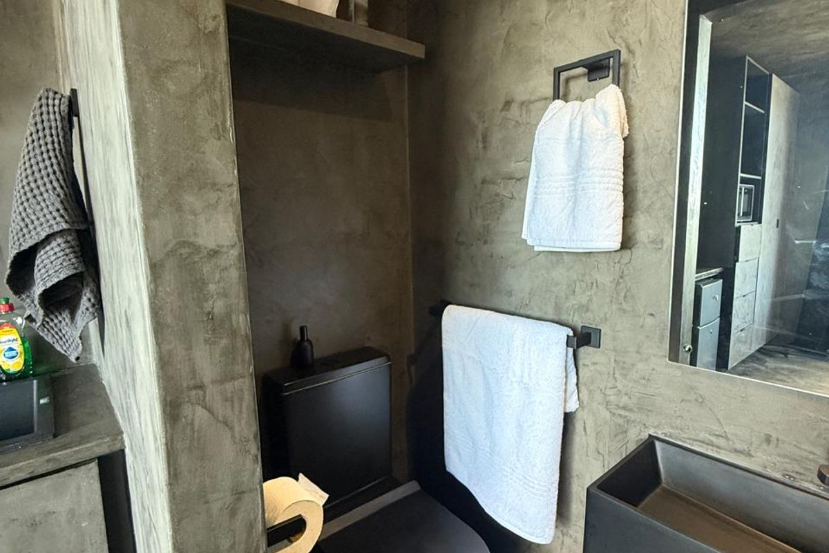 Modern bathroom featuring dark concrete-style wall finishes, a sleek black toilet, and a minimalist wall-mounted black basin with matching fixtures.