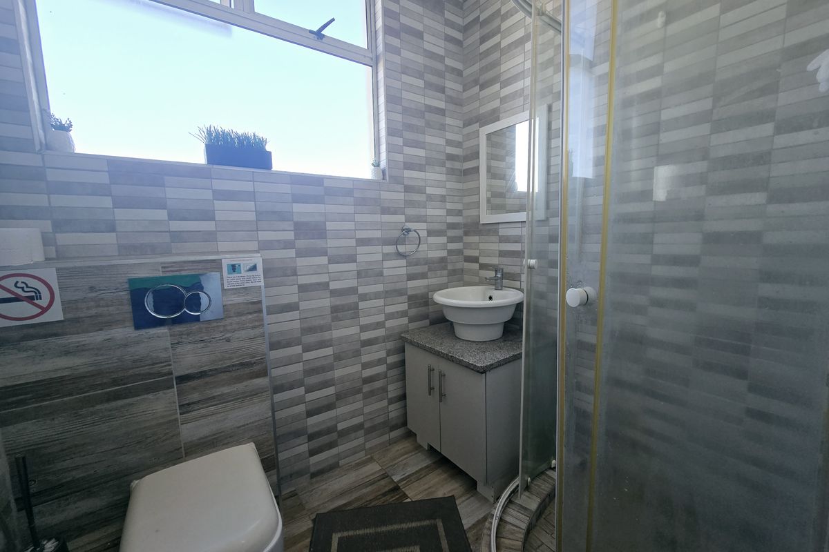 A compact bathroom featuring a wall-mounted toilet, a vessel sink with vanity cabinet, and a corner shower enclosure with tiled finishes.