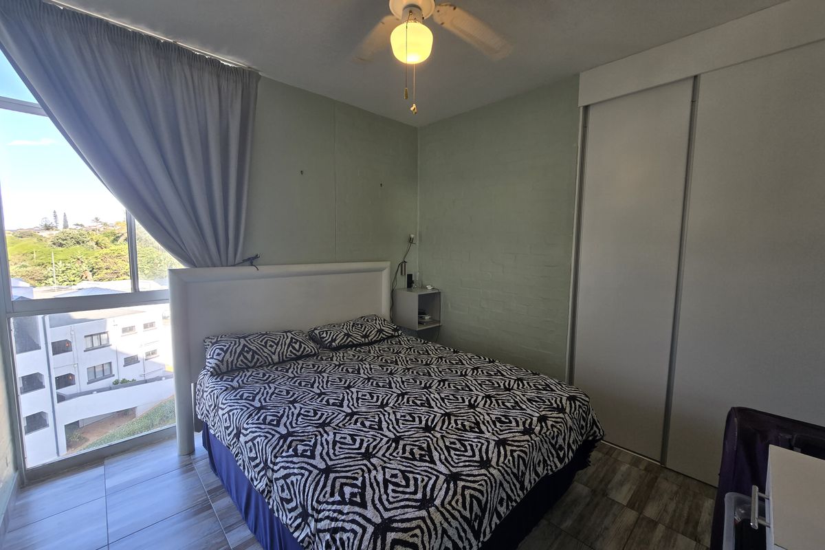 A bedroom featuring tiled flooring, a built-in wardrobe, a ceiling fan, and a large window offering natural light and exterior views.