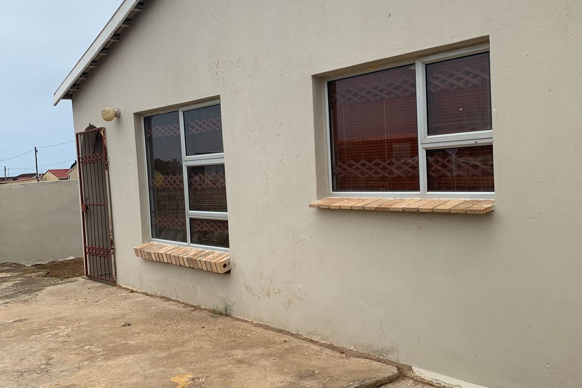 A view of the rear exterior facade featuring aluminium-framed windows with brick sills and a security gate, set against a concrete paved area.