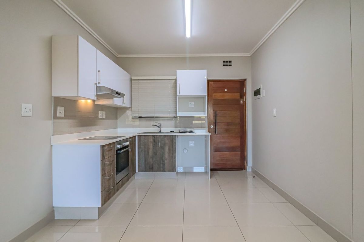 Modern kitchen featuring two-tone cabinetry, built-in oven and hob, tiled flooring, and direct access to the apartment entrance.