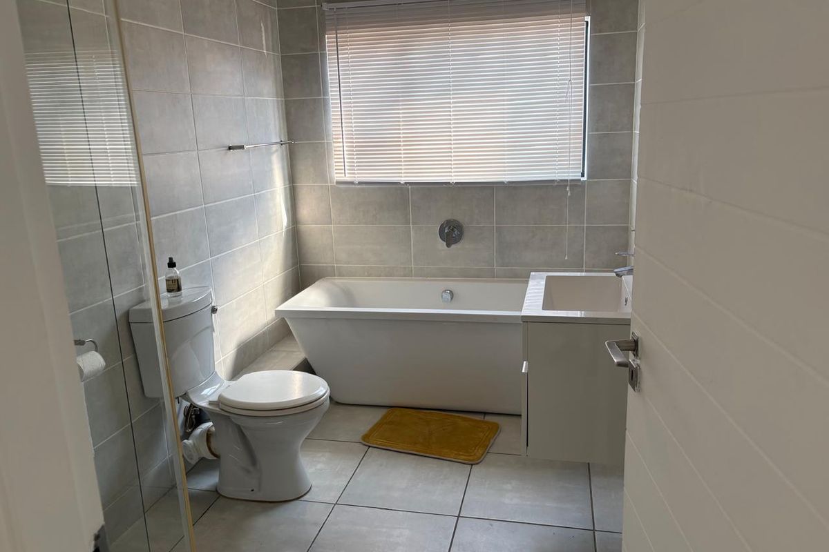 A modern bathroom featuring a freestanding bathtub, wall-mounted vanity, and neutral floor-to-ceiling tiling.