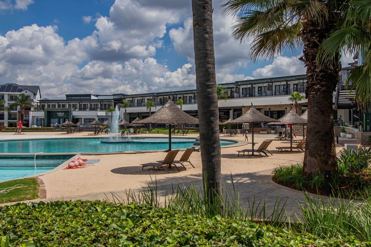 A well-maintained communal pool area featuring a large swimming pool, water fountain, paved walkways, and landscaped garden surroundings within the apartment complex.