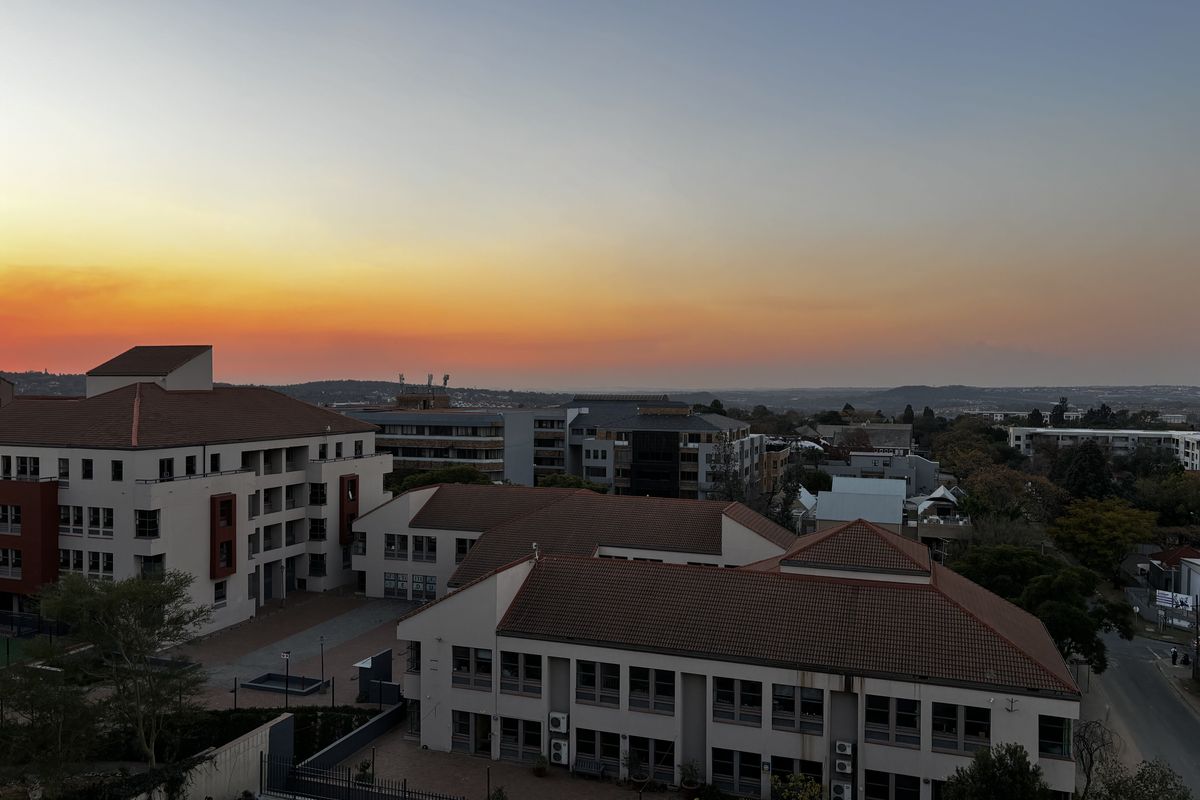An elevated aerial view of the apartment complex at sunset, showcasing the building architecture, tiled roofing, and surrounding neighbourhood landscape.