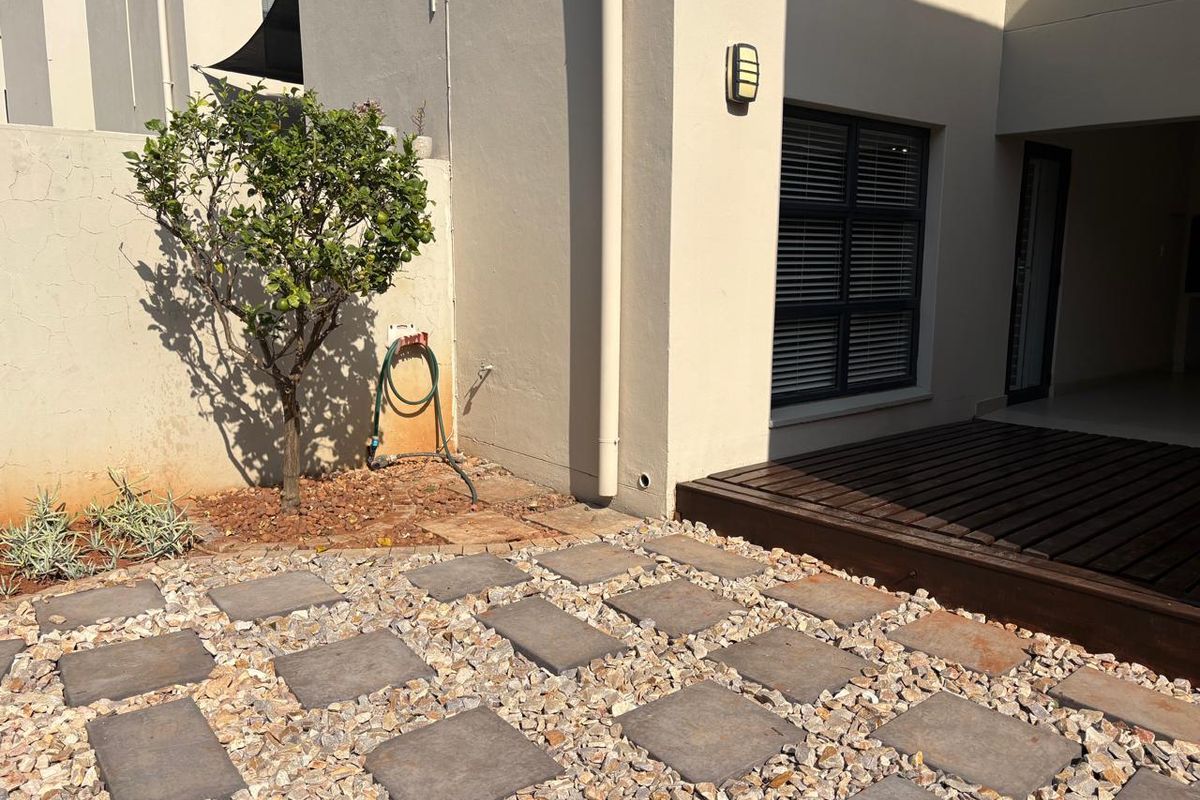 A low-maintenance rear courtyard featuring a timber deck, stone paving, and a boundary wall with integrated exterior lighting.