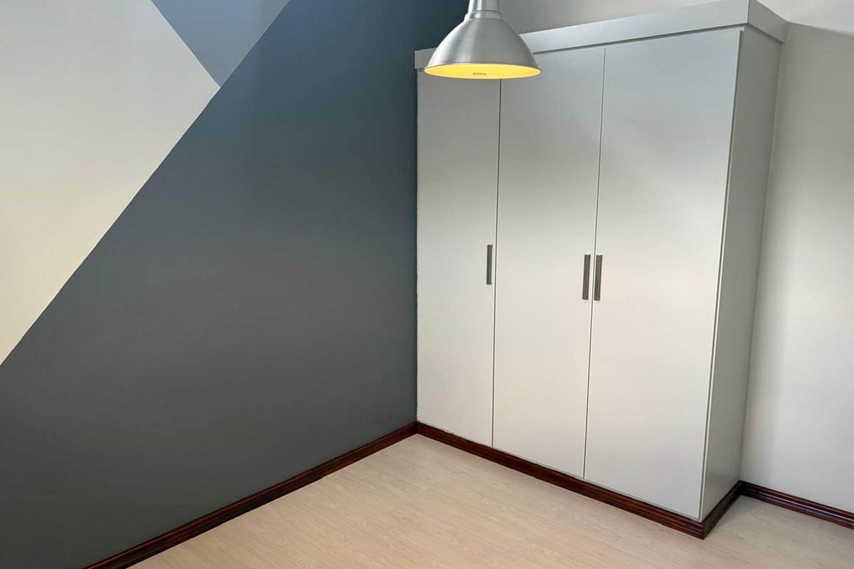 A bedroom featuring light wood-look flooring, a built-in wardrobe, and a modern geometric accent wall.