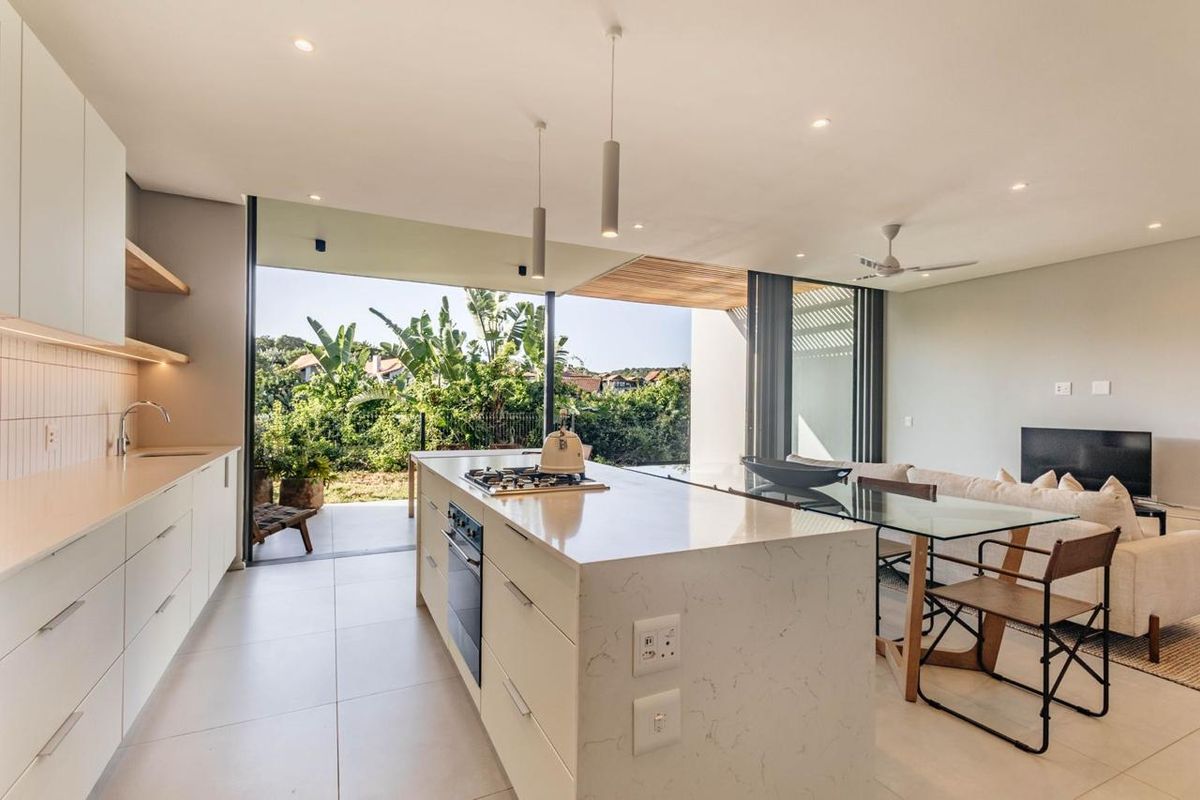 Modern open-plan kitchen and living area featuring a central island, stone countertops, and seamless indoor-outdoor flow through large sliding glass doors to the patio.