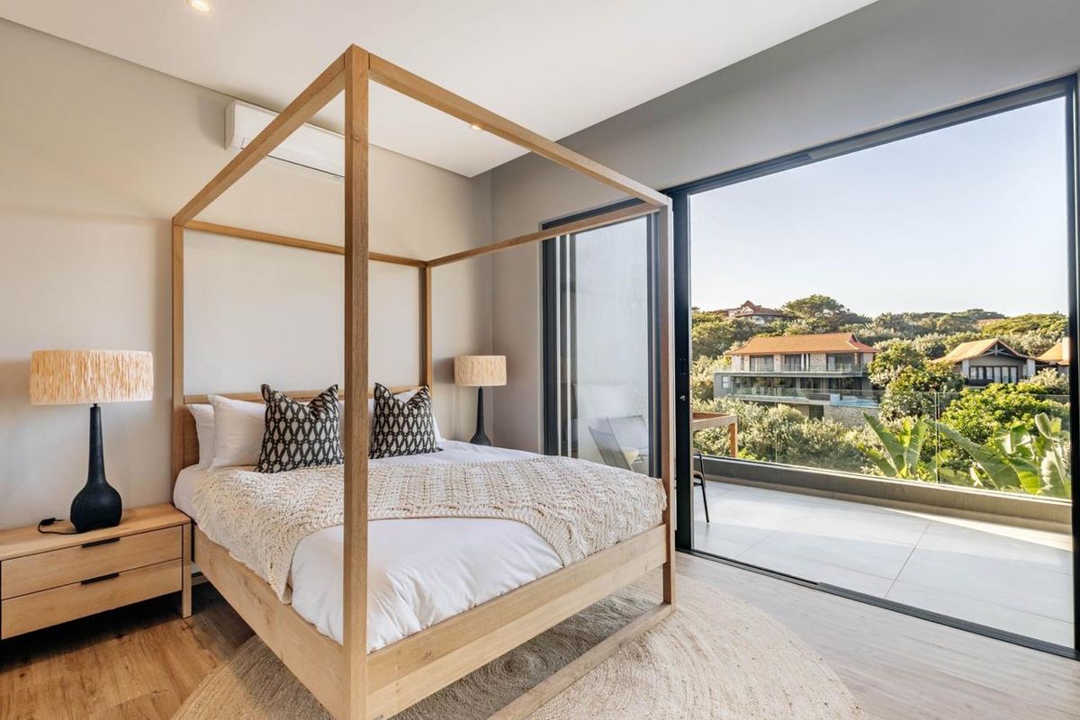 Modern bedroom featuring light wood flooring, recessed lighting, and large sliding glass doors opening onto a private balcony with scenic views.