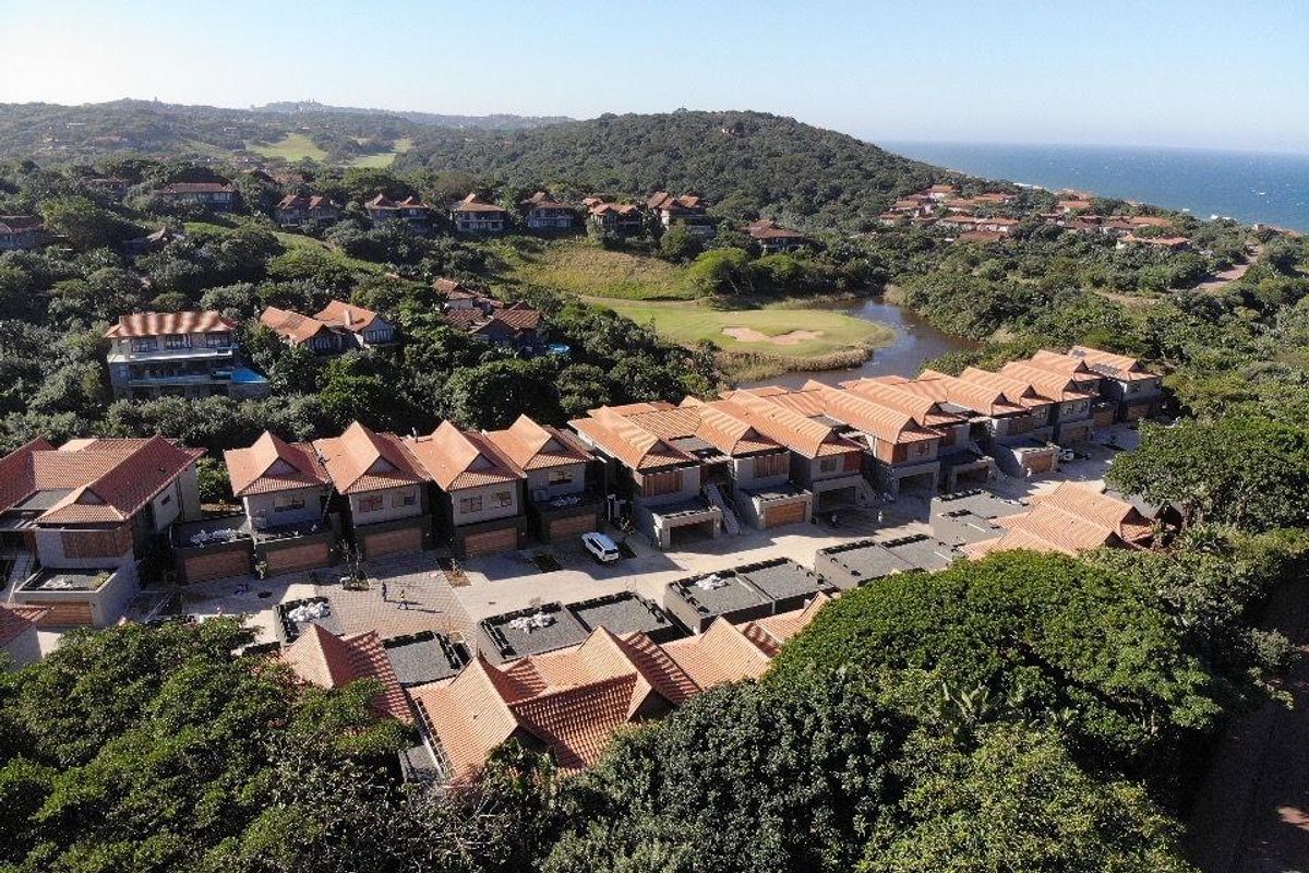 An aerial view of a townhouse complex featuring terracotta tiled roofs, paved driveways, and garages, set within a lush coastal estate environment.