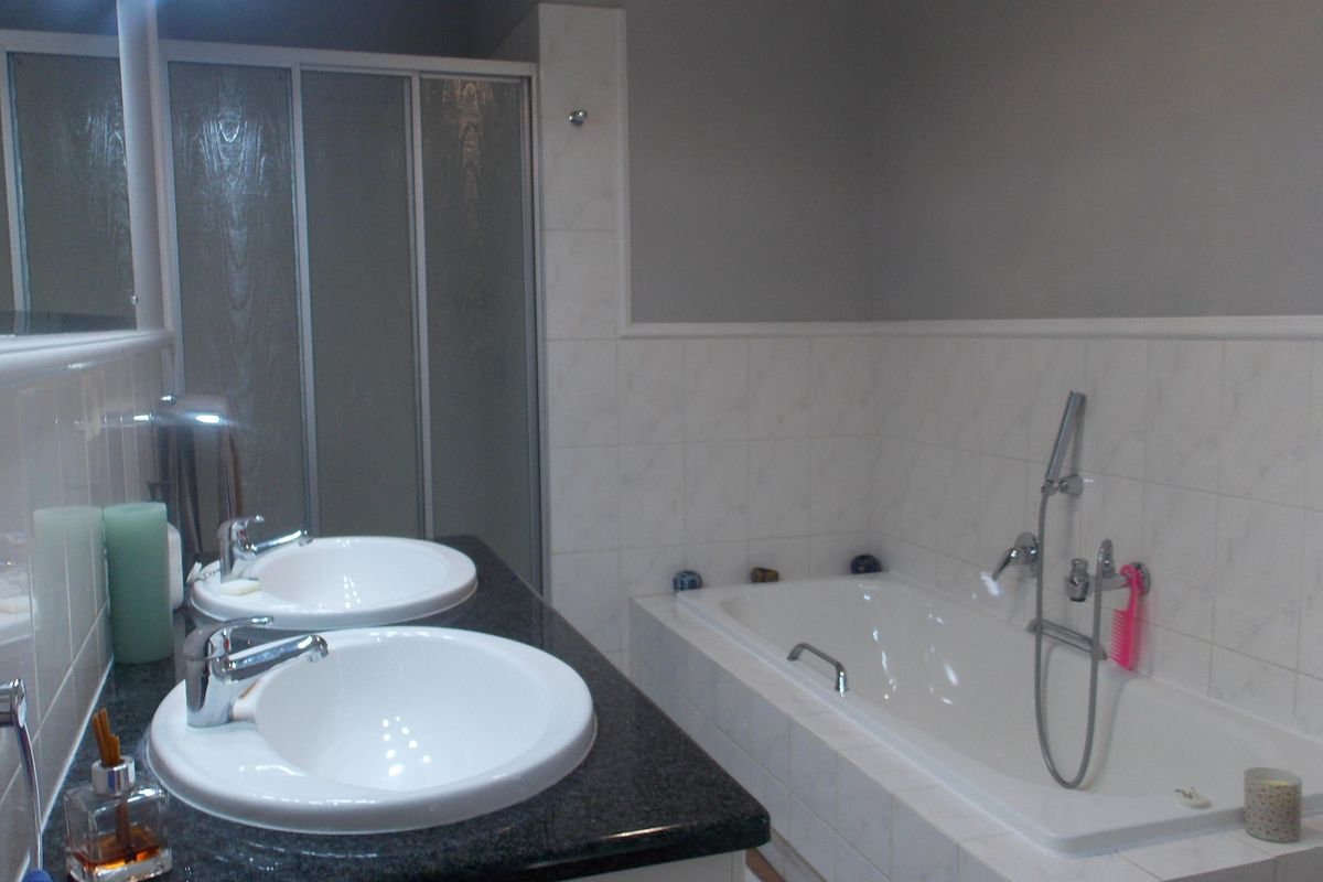 A functional bathroom featuring a double vanity with granite countertop, a built-in bathtub with shower attachment, and a separate glass-enclosed shower stall.