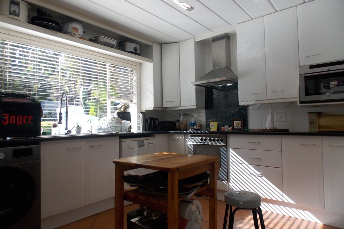 A functional kitchen featuring white cabinetry, dark countertops, a stainless steel extractor fan, built-in oven, and tiled flooring with natural light.