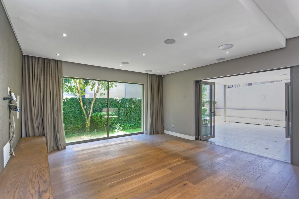 Spacious living area featuring hardwood flooring, recessed ceiling lighting, integrated sound system speakers, and large sliding doors opening onto a paved patio and garden.