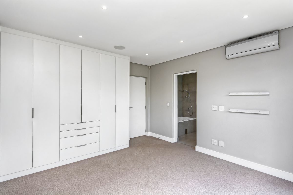 A well-maintained bedroom featuring built-in cupboards, neutral carpeting, recessed lighting, an air conditioning unit, and an en-suite bathroom.