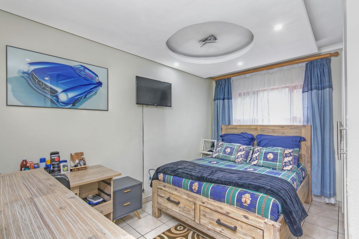 A bedroom featuring tiled flooring, a recessed ceiling detail with integrated lighting, and a window with curtain tracks.