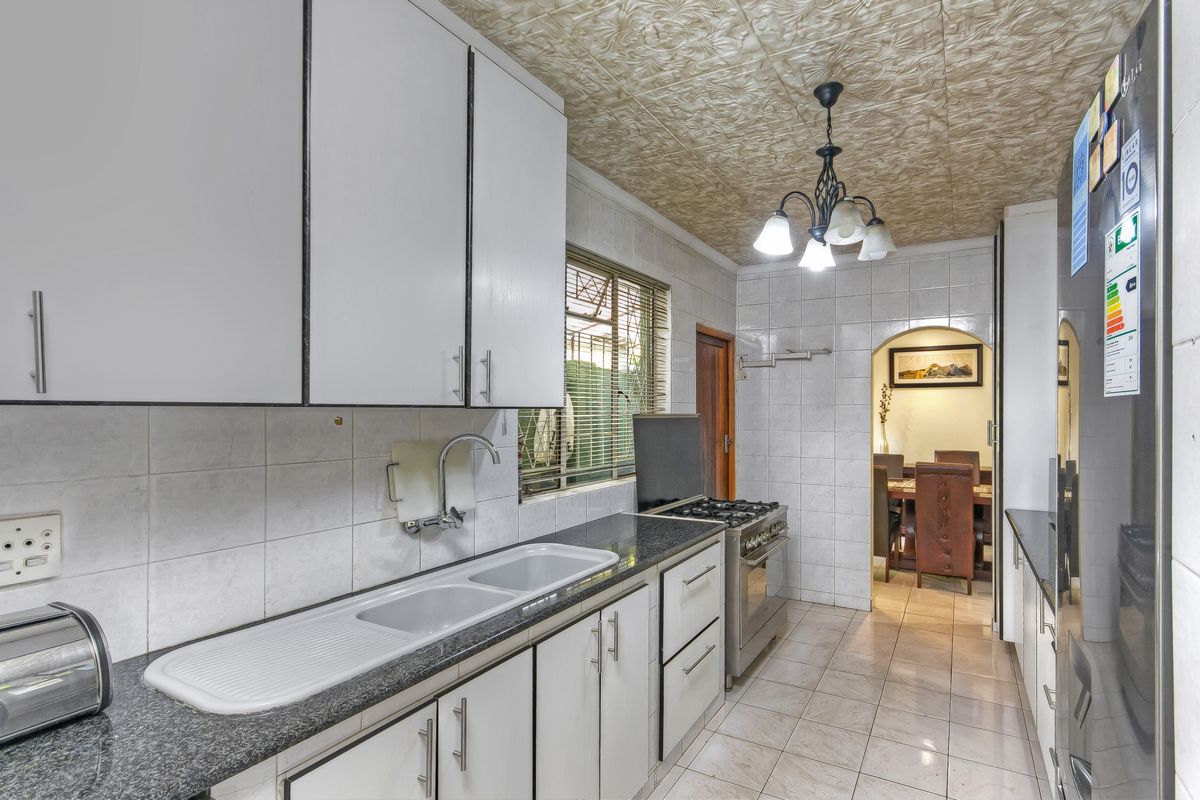 A functional kitchen featuring white cabinetry, granite countertops, a double sink, and a freestanding gas stove, with an arched doorway leading to the dining area.