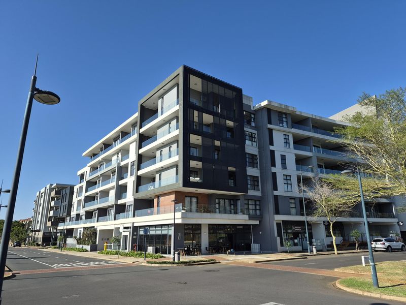 A modern multi-story apartment building featuring contemporary architectural design, glass balconies, and ground-floor commercial space, situated on a corner street intersection.