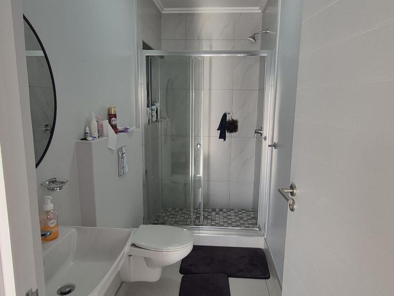 A modern bathroom featuring a wall-mounted toilet, a sleek vanity basin, and a glass-enclosed shower with tiled finishes.