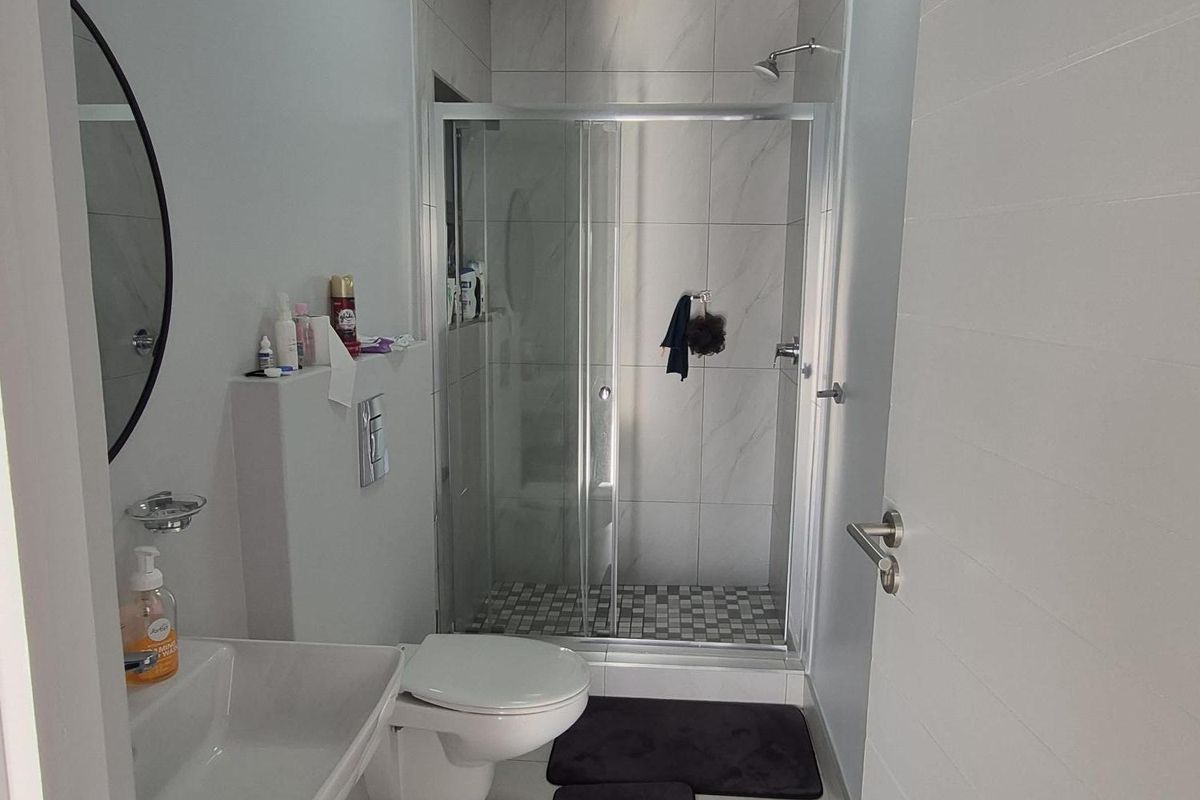 A modern bathroom featuring a wall-mounted toilet, a sleek vanity basin, and a glass-enclosed shower with tiled finishes.